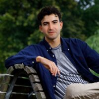 Columnist Bas Rooijakkers zit op een bankje.