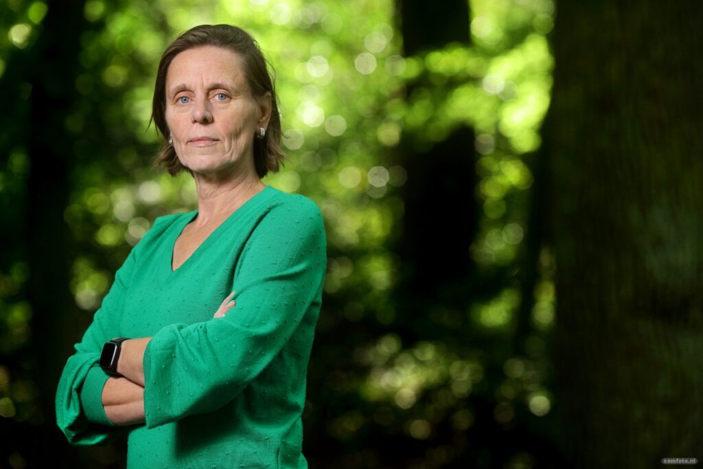 Daphne Stam’s resignation: ‘I was primarily seen as a female academic’ Links in beeld, met haar armen over elkaar en haar lichaam gericht naar links, staat een vrouw met halflang haar en een groene trui. Dat is Daphne Stam. Ze kijkt serieus de camera in. Op de achtergrond staan, wazig, bomen.