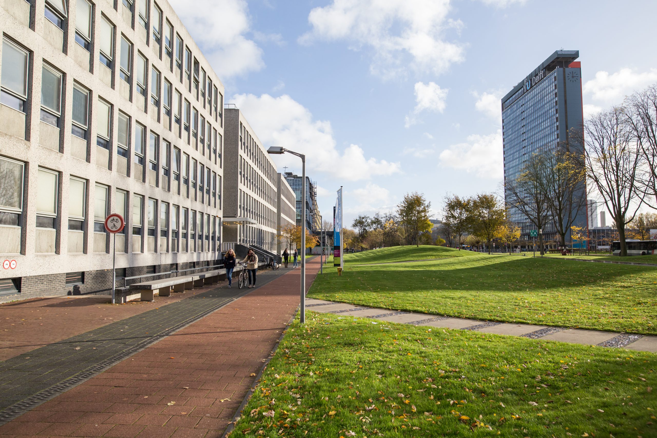 Brainstorm sessie over inrichting TU-campus Landschapsfoto, met links een wit gebouw, naast een rood fietspad. Rechts van het fietspad is een grasveld. Rechts in de verte is een hoog gebouw zichtbaar met bomen ervoor.